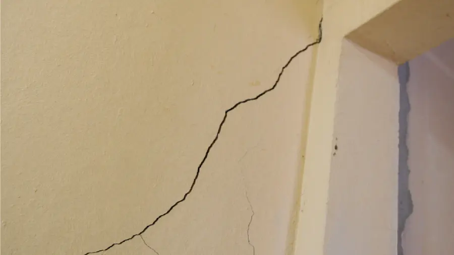 Parede bege com uma fissura diagonal partindo do canto de uma porta
